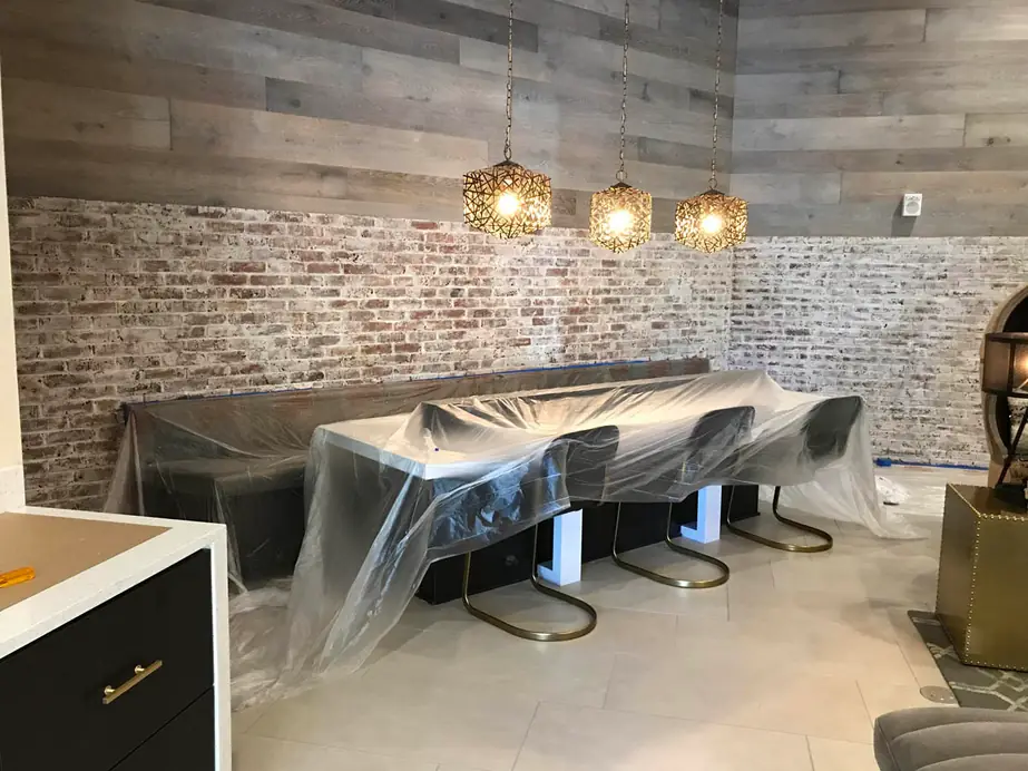 The same dining nook mid-prep, table, bench and stools wrapped in plastic sheeting before the brick was whitewashed
