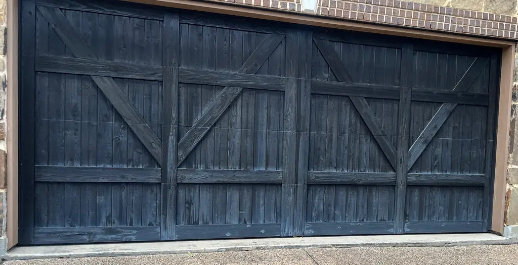 Wood garage door in a black stain with X-bracing, set in a brick and stone surround
