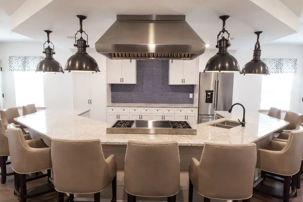 Kitchen with a stainless hood, four pendants, white shaker cabinets and a curved stone island