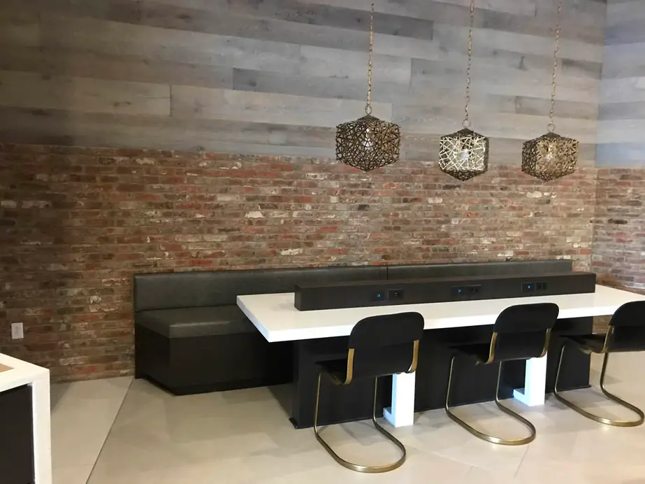 Finished dining nook with a whitewashed brick feature wall, grey plank wall, bench seating and brass pendants