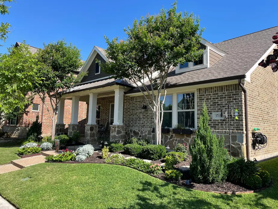 Craftsman house with freshly painted white porch columns, gable and trim over Austin stone, with a mown lawn and planted beds