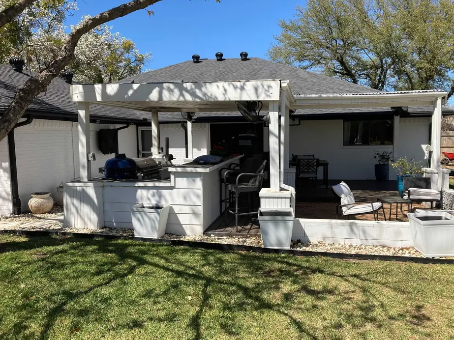 Outdoor kitchen and pergola painted white against brick, under Texas live oaks
